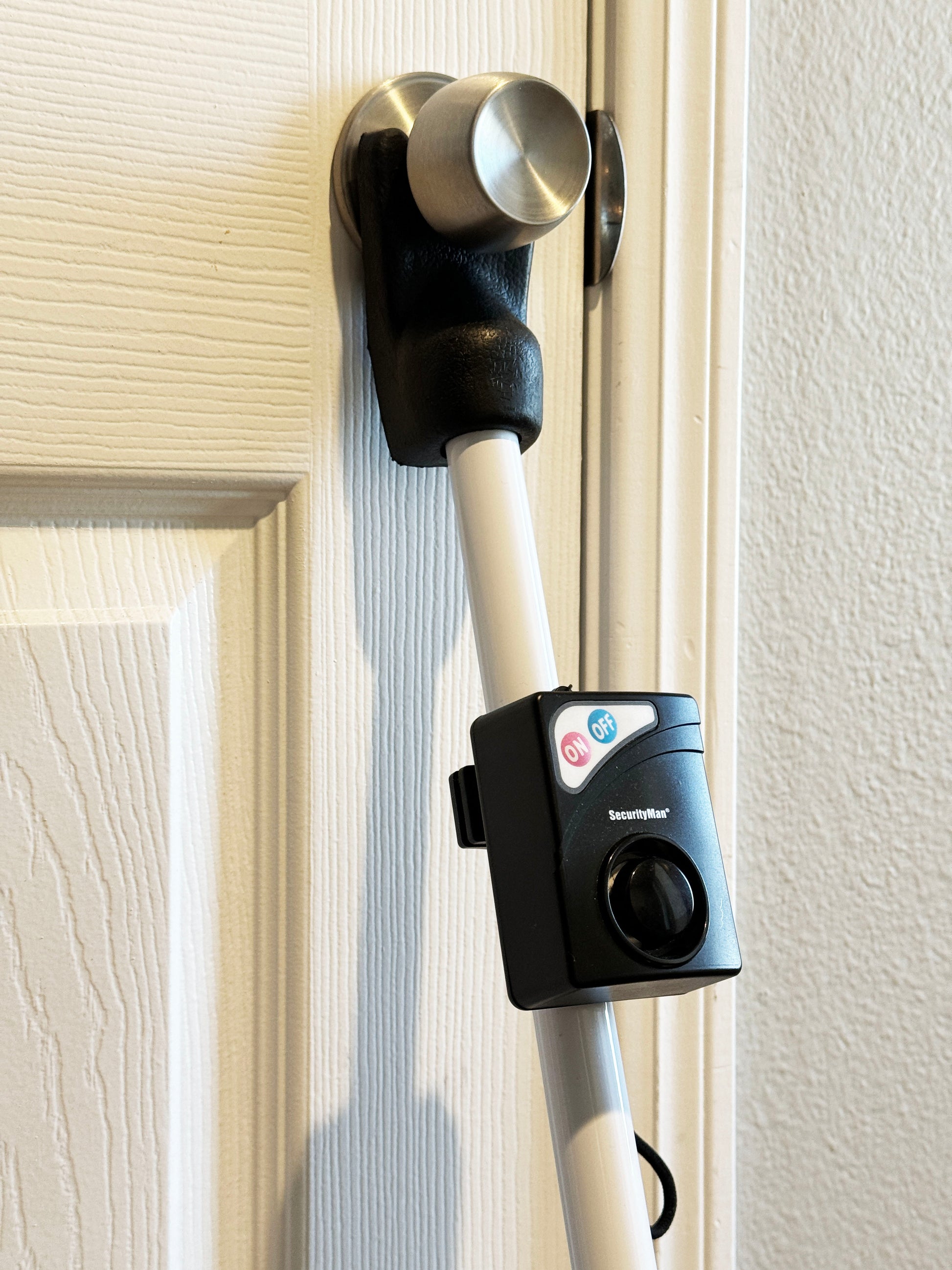SecurityMan door security bar with alarm installed under door knob on hinged door showing rubber grip and alarm module in use